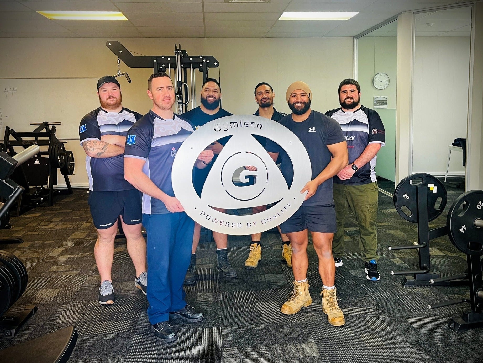 Guys holding a Gymleco sign inside of their gym.