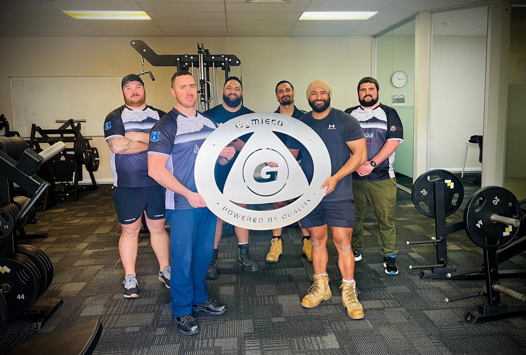 Guys holding a Gymleco sign inside of their gym.