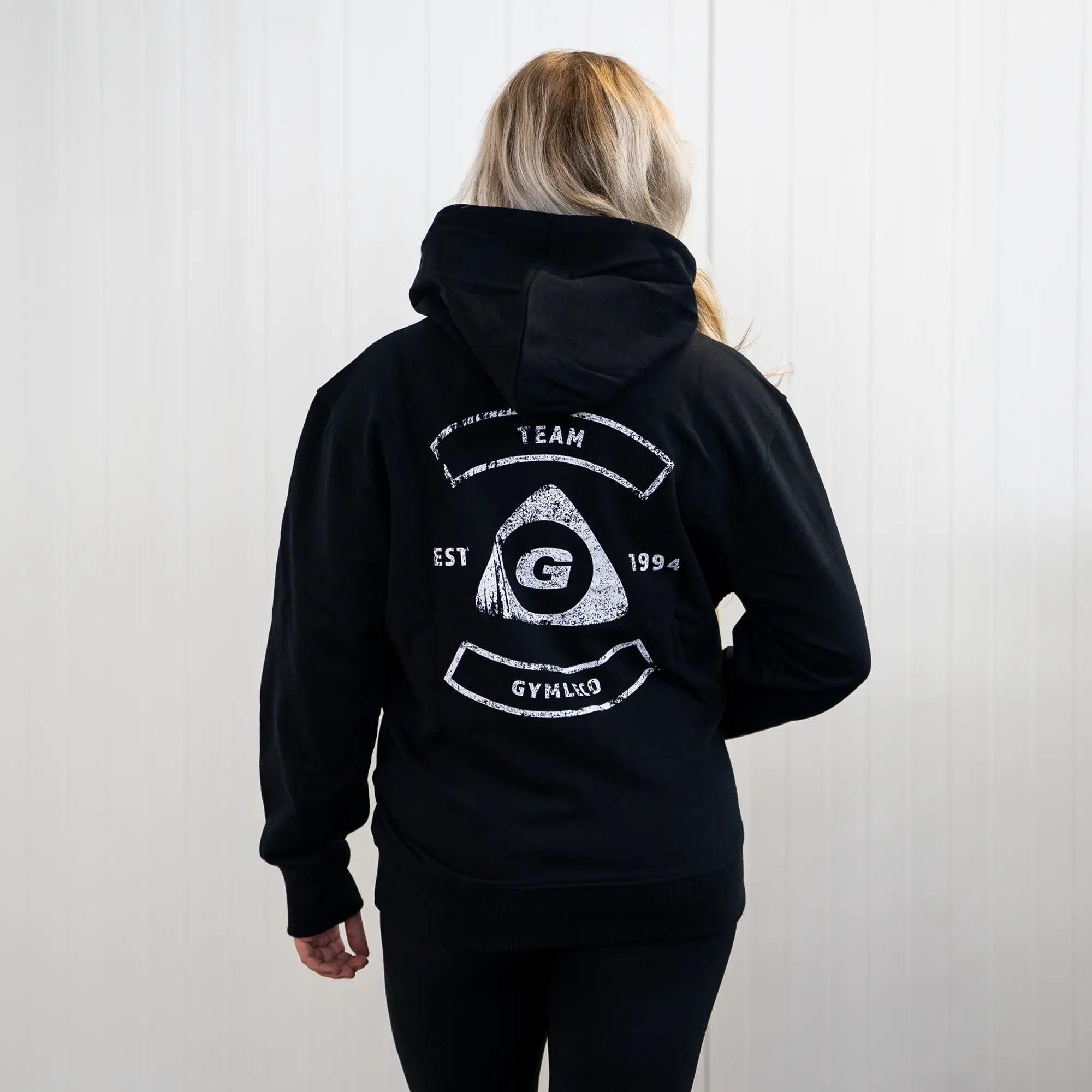 Person wearing a black hoodie with a logo and text on the back against a white background