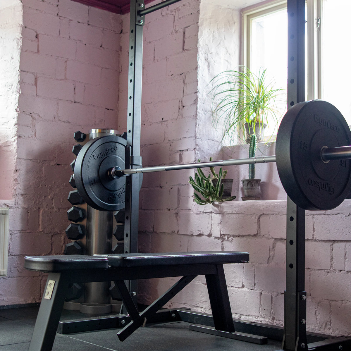 Weightlifting bench with barbell in a room with pink walls and a window.