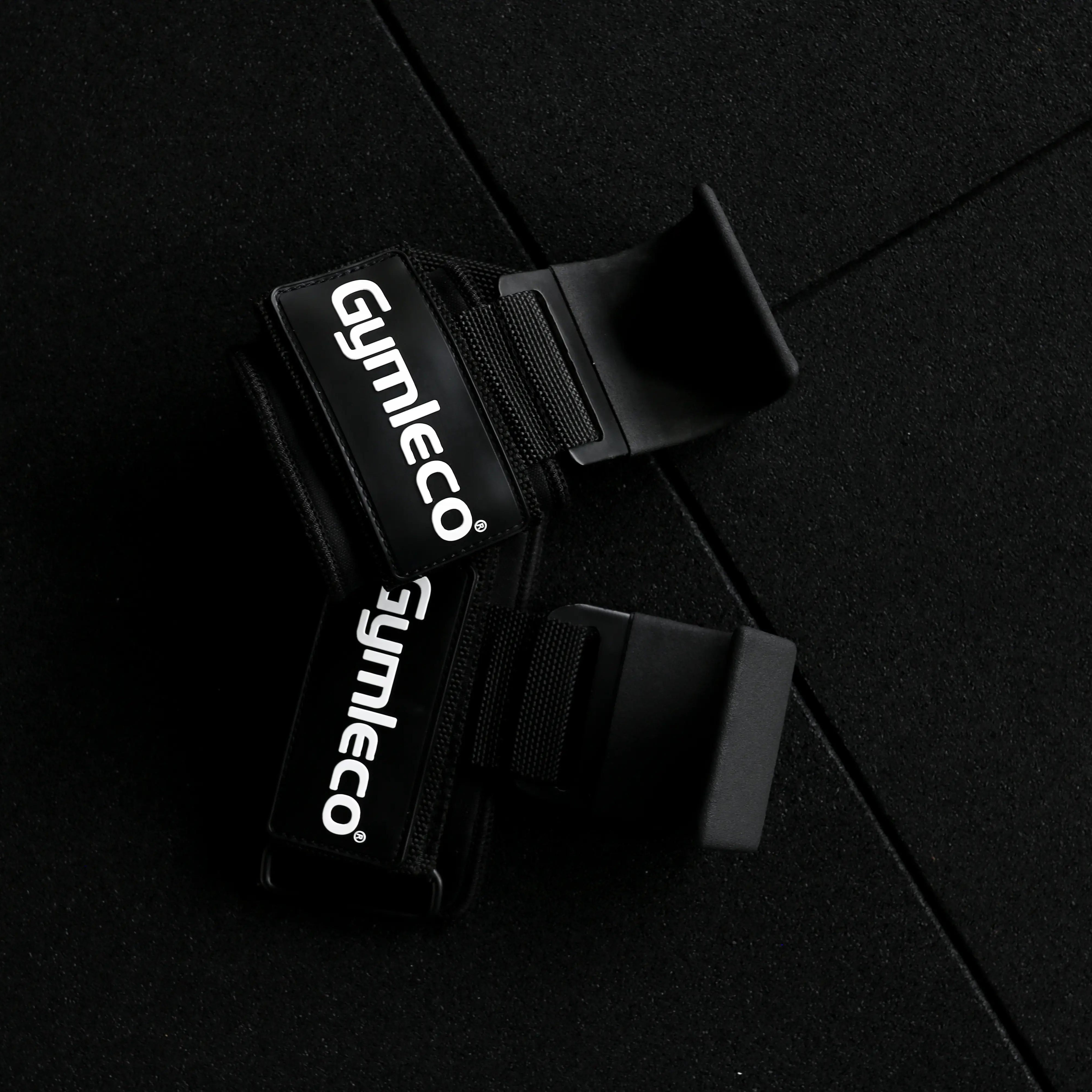 Black Gymleco wrist wraps with white brand lettering, shown on a dark textured background.