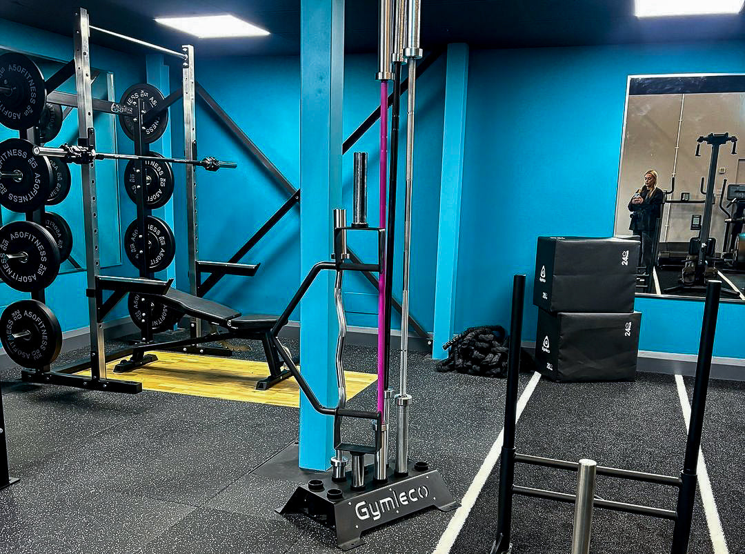 A blue gym with Gymleco barbells and free weights.