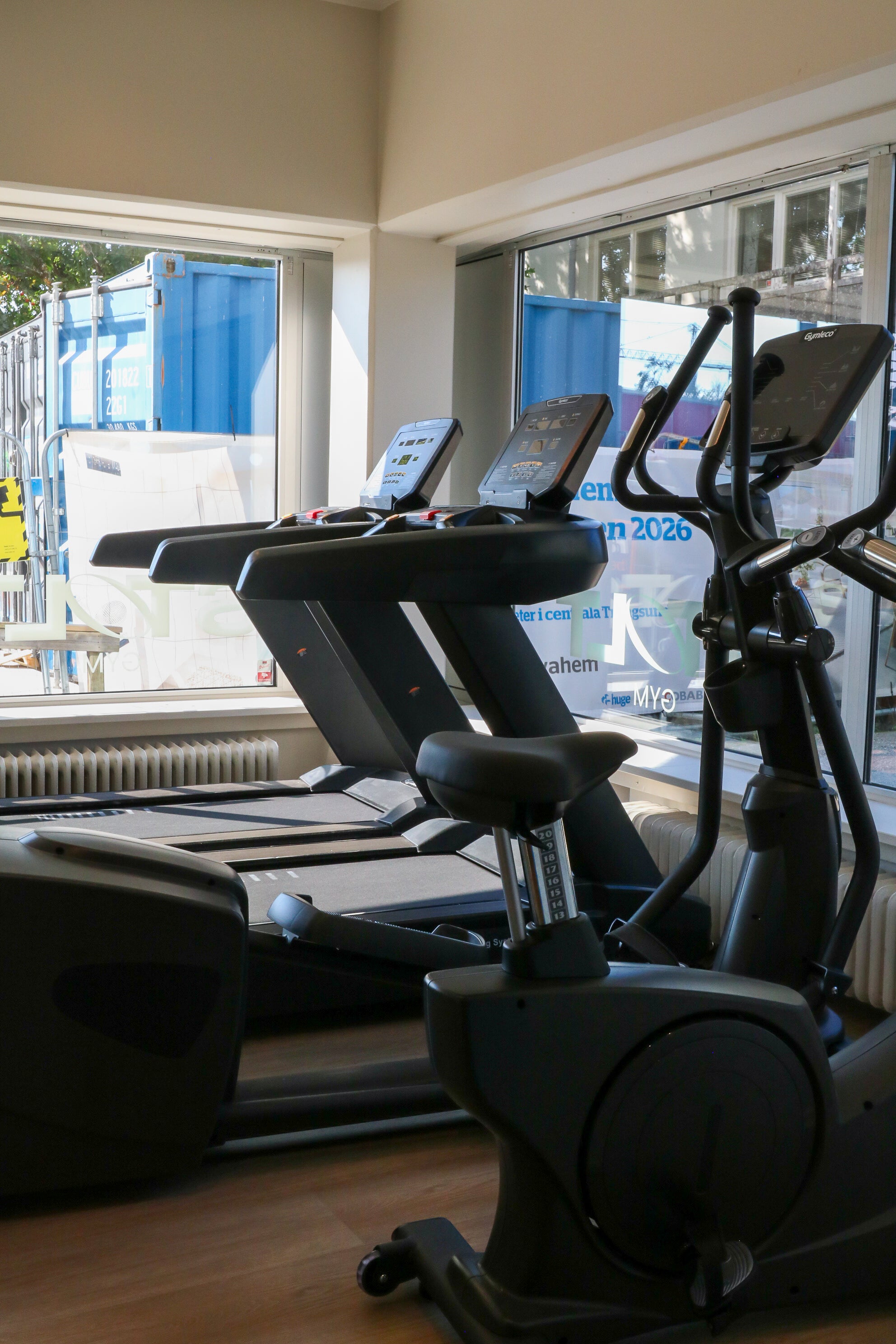 Gymleco equipment including treadmills and elliptical machines with large windows in the background.