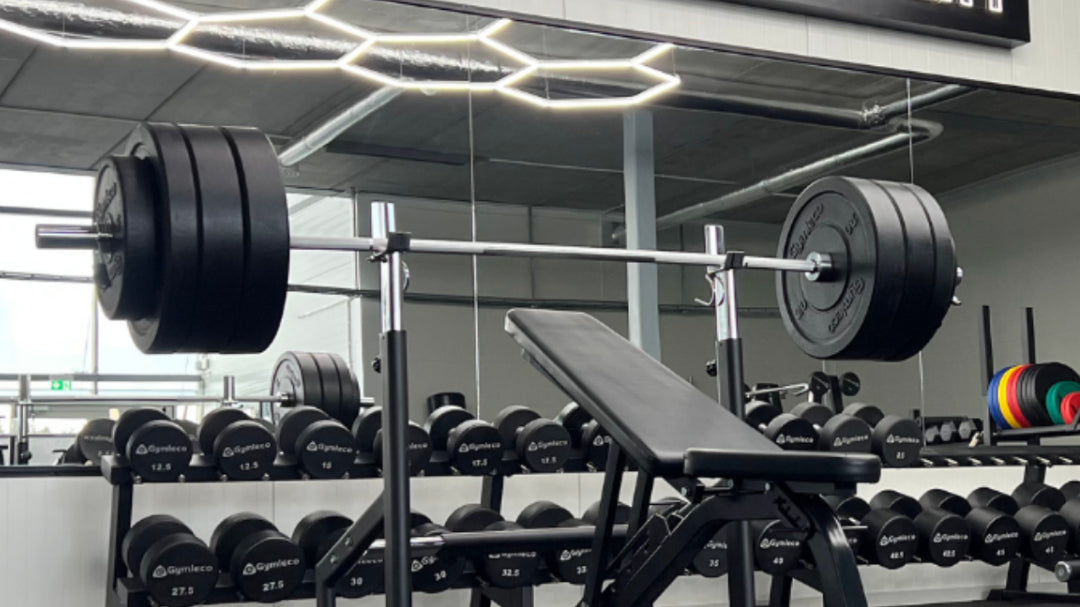Gym interior with weightlifting equipment and 'Powered by Quality' sign.