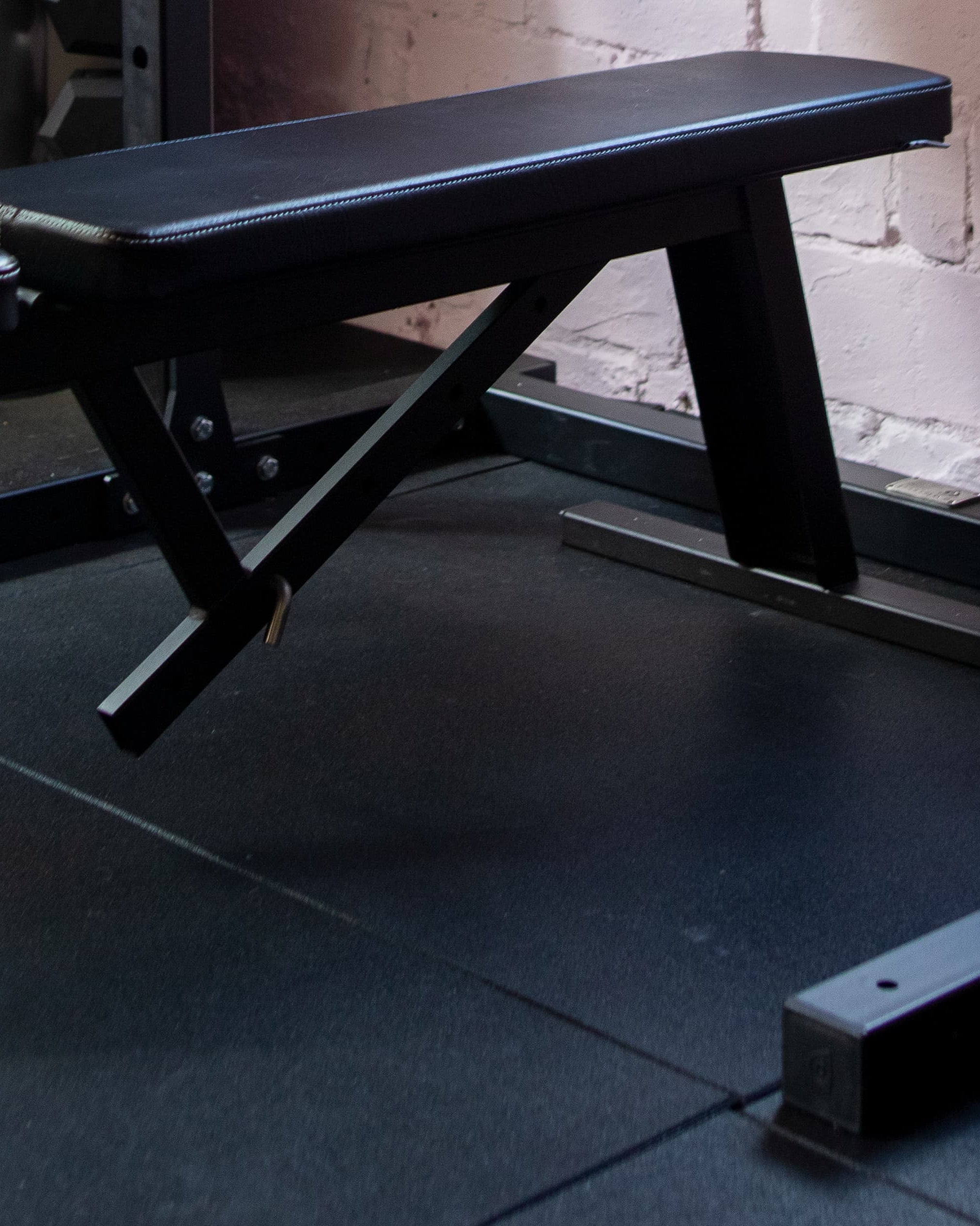 Black weight bench in a gym setting with a brick wall background
