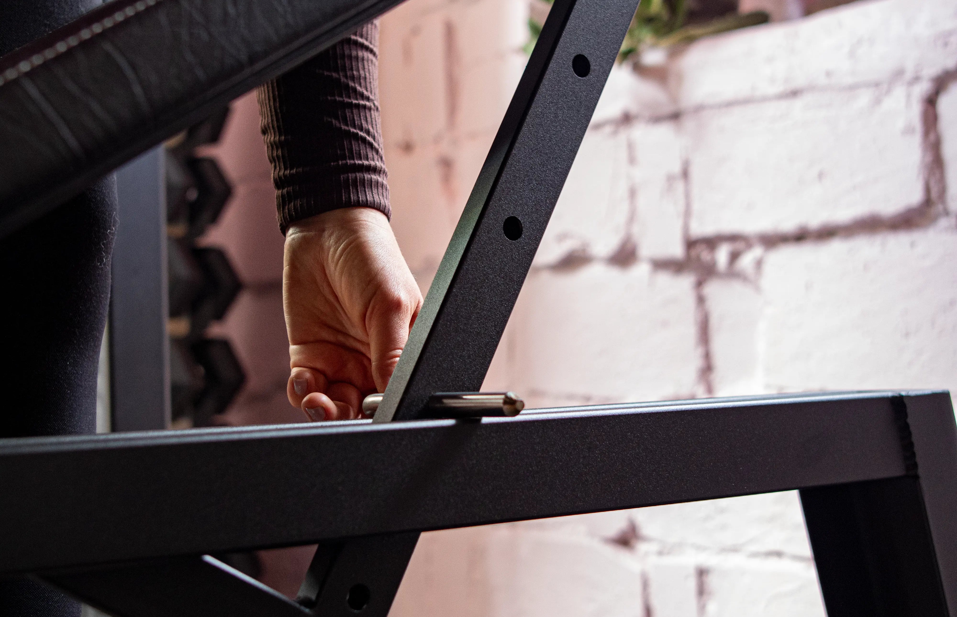 Person assembling a black metal frame on a bench with a blurred background