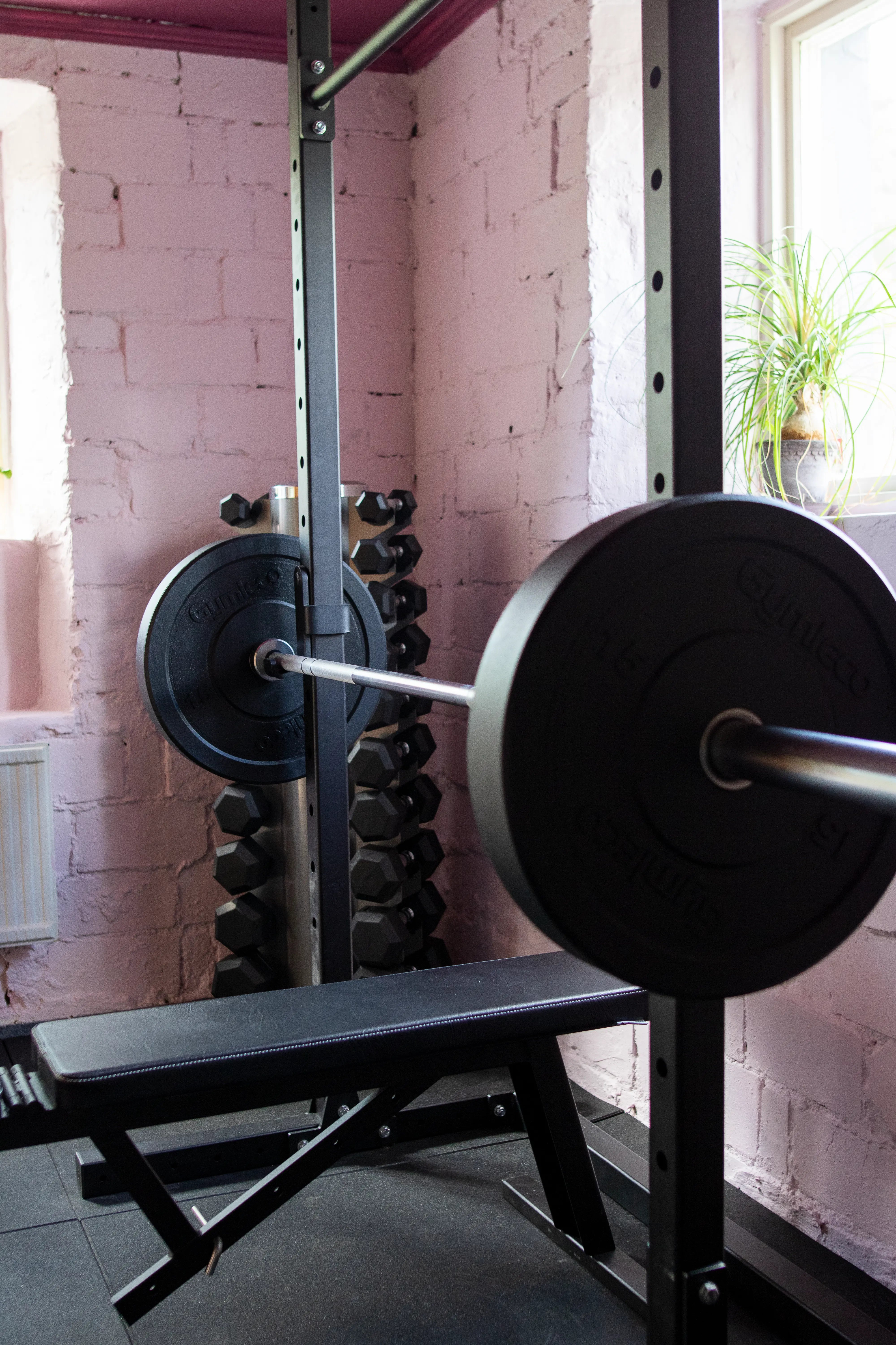 Barbell with weights on a rack in a gym setting with pink brick walls.