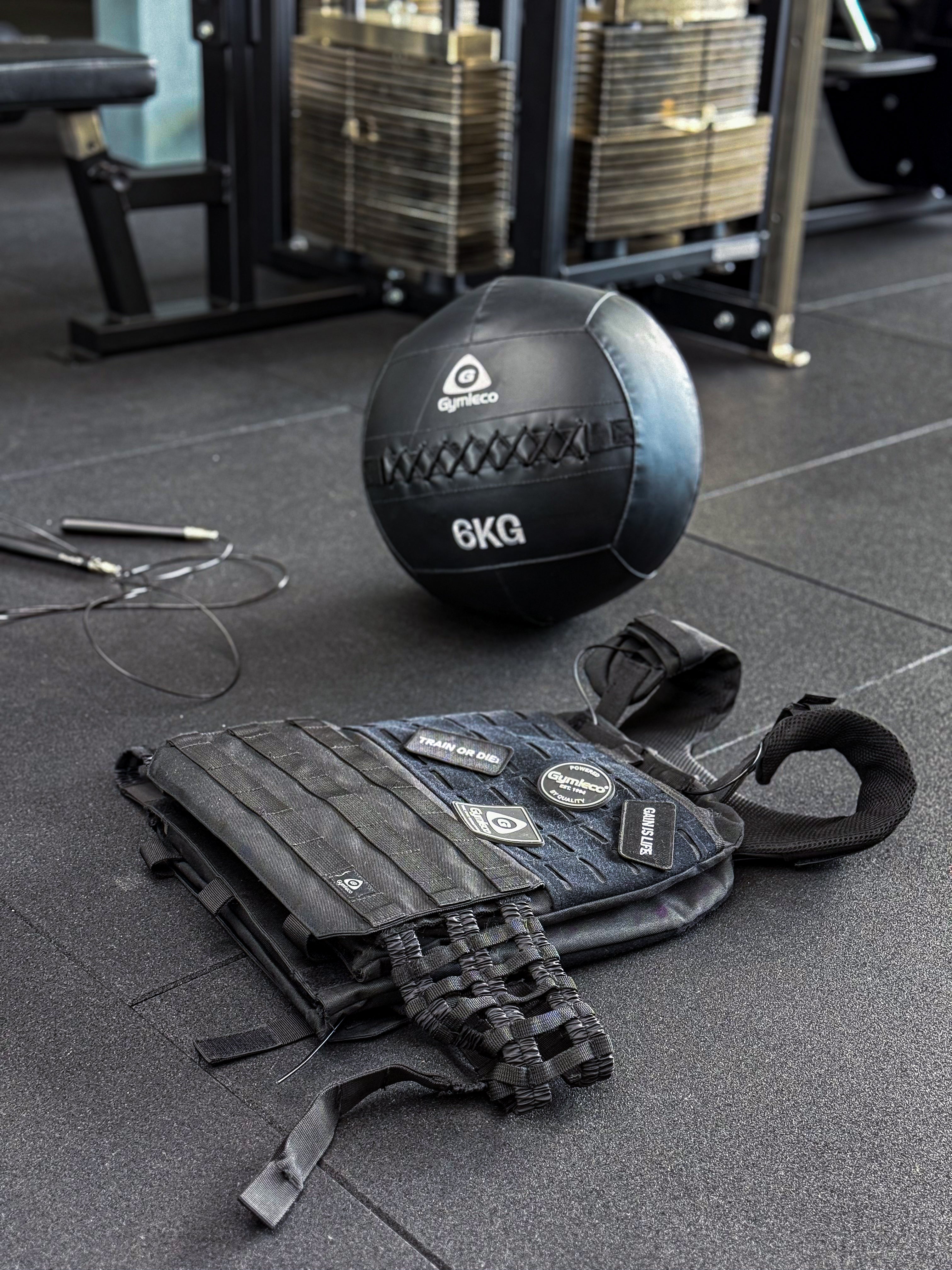 A weight west with patches, laying on the ground. A medicine ball and jumping ropes in the back.