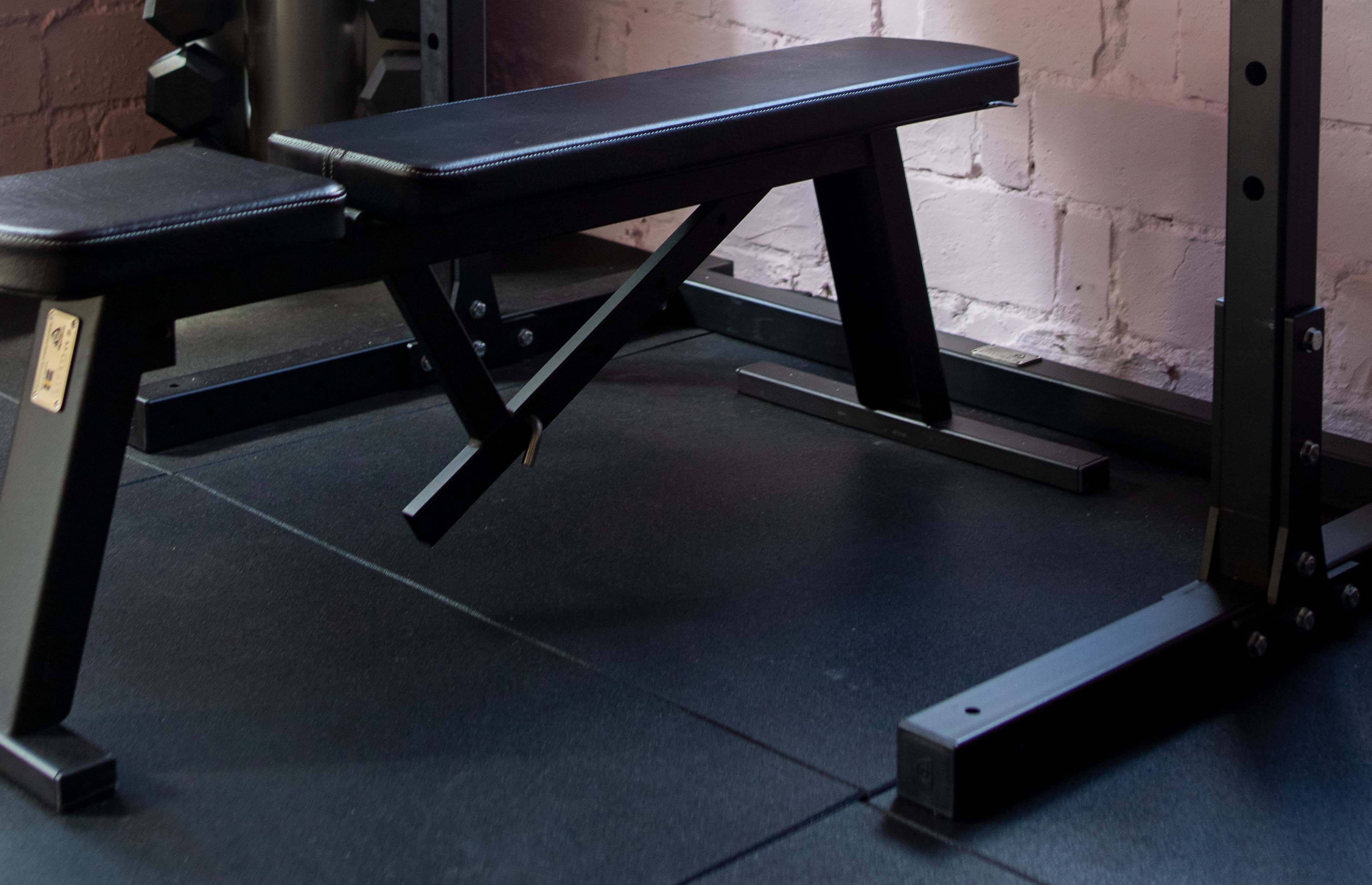 Black weight bench in a gym setting with a brick wall background